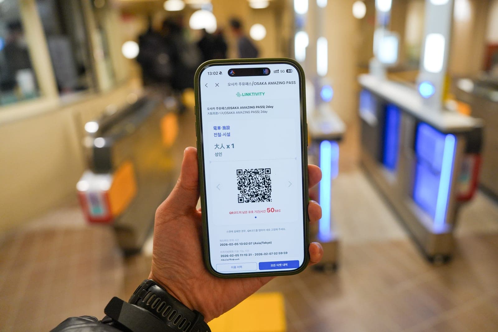 Osaka Amazing Pass 2-day QR voucher on a phone, held up in front of subway gates