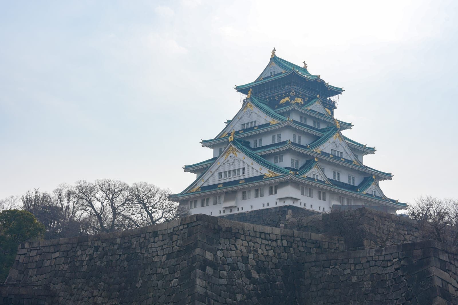 Osaka Castle Tenshukaku exterior, white walls and green tiled roof rising above massive stone walls
