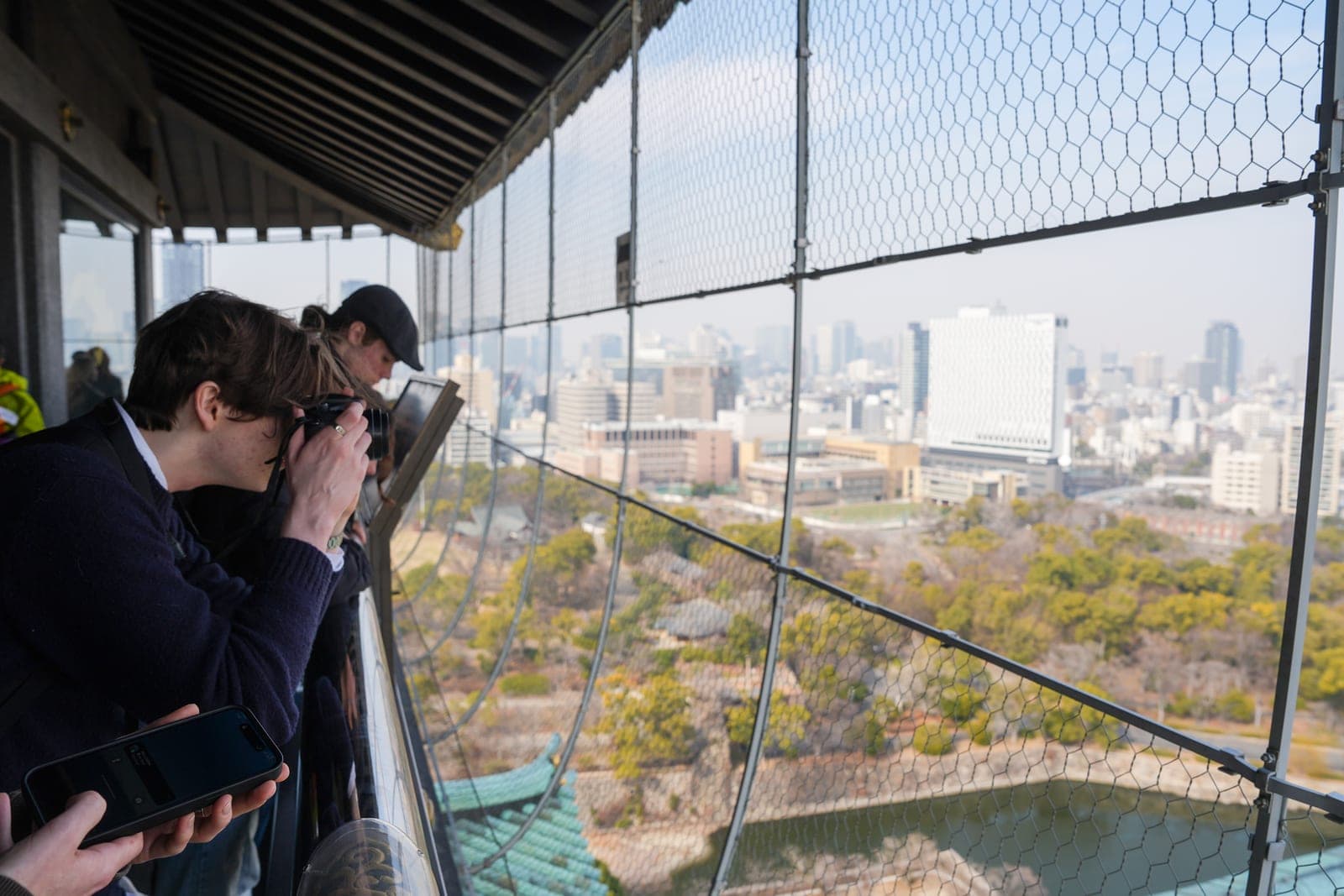 View from the 8th-floor observation deck of Osaka Castle Tenshukaku, with safety mesh framing the north Osaka skyline
