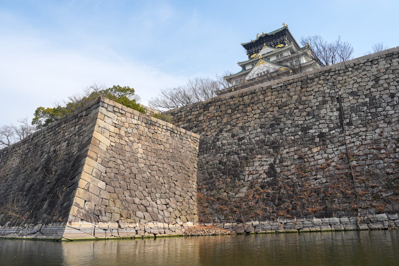 Osaka Castle Tenshukaku seen from the moat, with the keep rising above the stone walls and water in the foreground