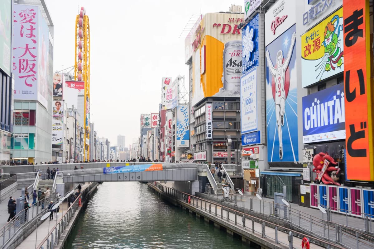 Dotonbori canal with the Glico running man sign and neon billboards by day