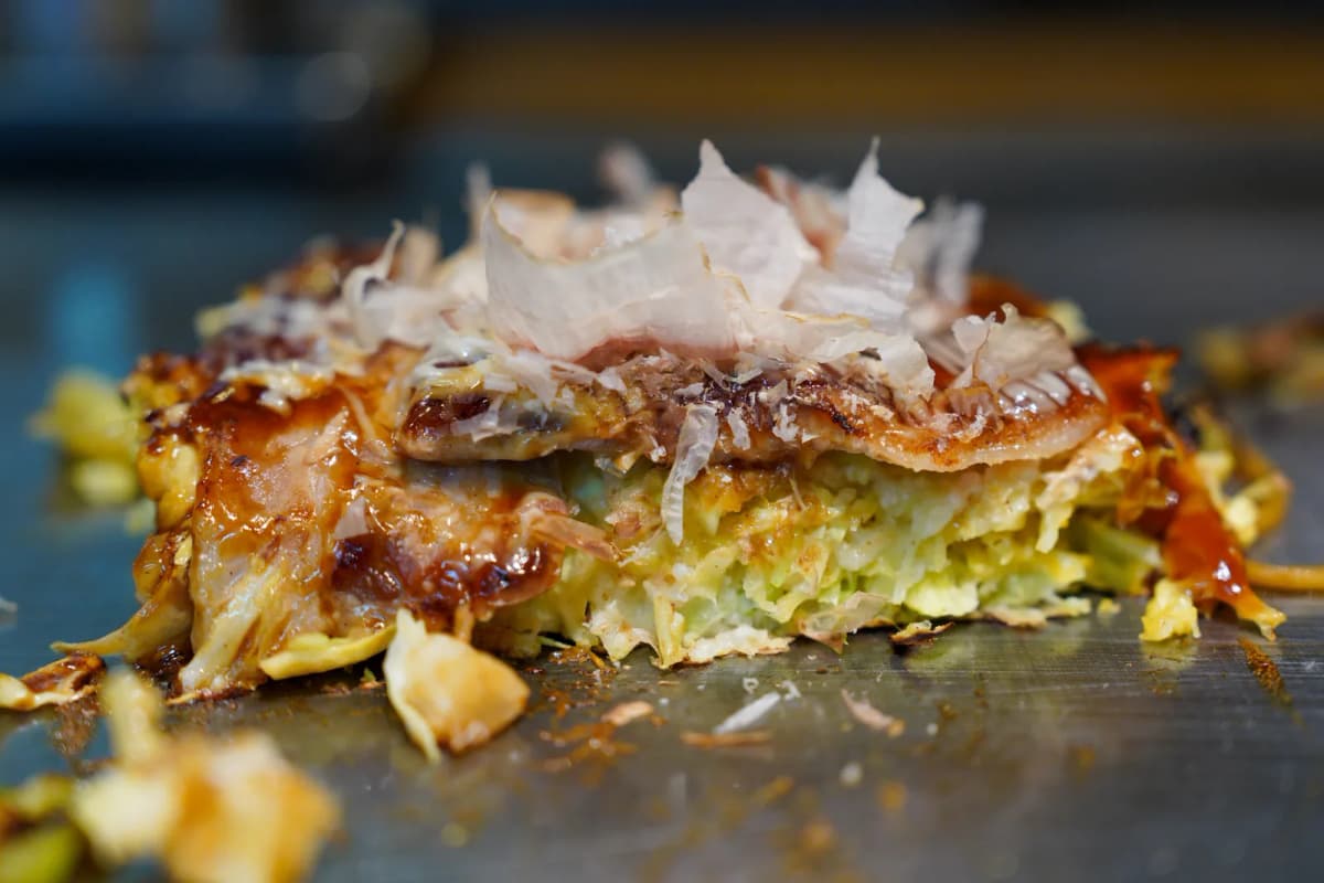 Pork okonomiyaki topped with bonito flakes on the griddle at Takekurabe in Namba