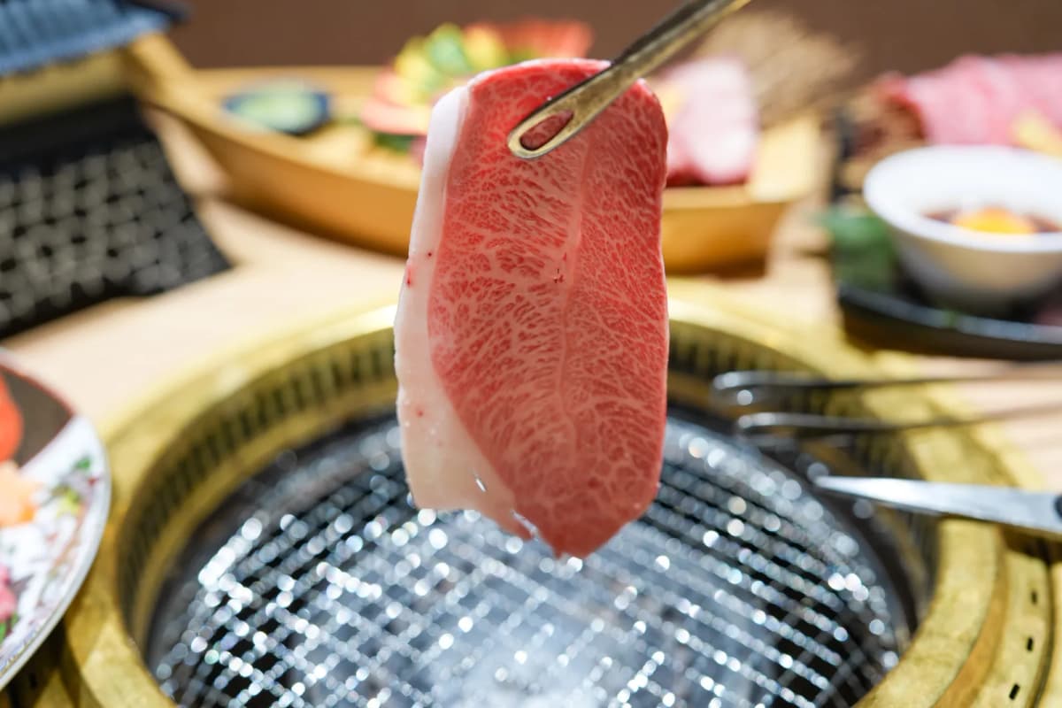 A slice of marbled black wagyu held over the grill at Yakiniku Sakon Dotonbori