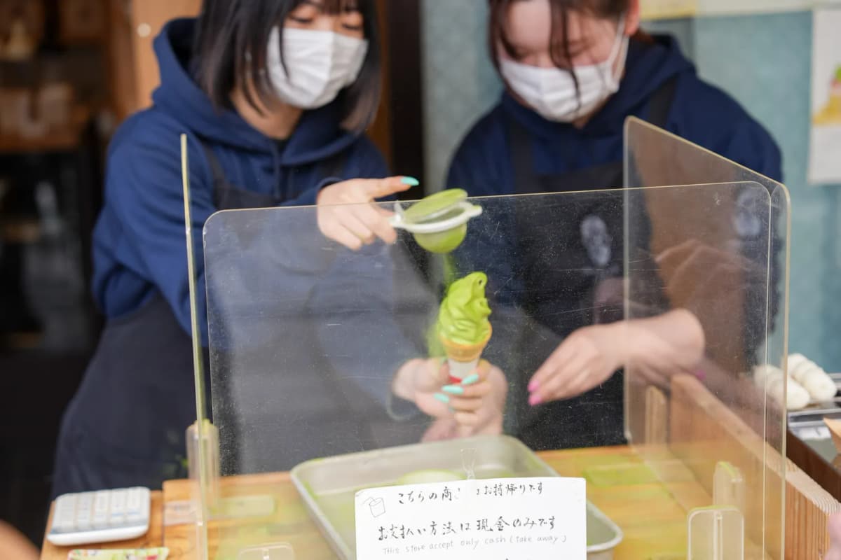 Staff dusting matcha powder over a matcha soft serve cone at a shop in Uji